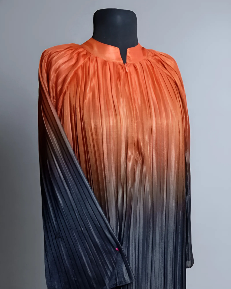 The Pleated Cascade Abaya in Sunset Haze. An elegant, silky abaya with an orange to black gradient and full-length pleats. Perfect for evening wear.