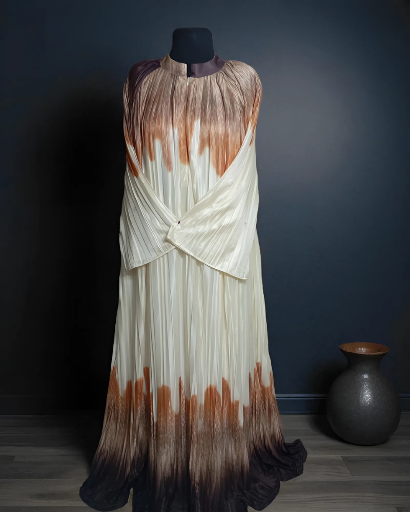 The Pleated Cascade Abaya in Sandstone. A luxurious, pleated abaya in a beige and brown gradient with a silky, fluid drape.