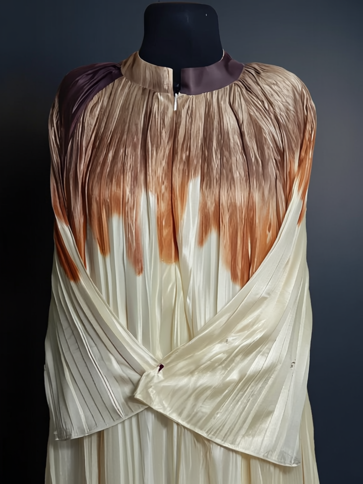 The Pleated Cascade Abaya in Sandstone. A luxurious, pleated abaya in a beige and brown gradient with a silky, fluid drape.